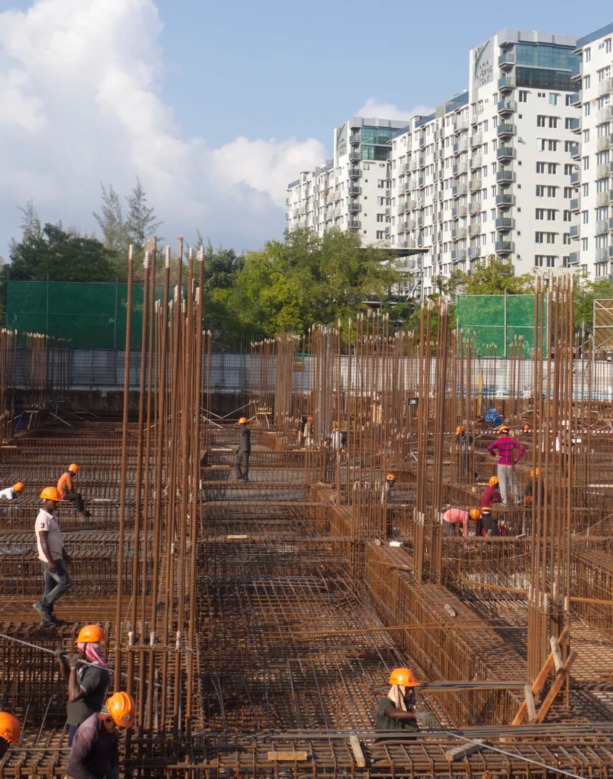 Crew tying reinforcement on a slab under construction, high-rise blocks behind.
