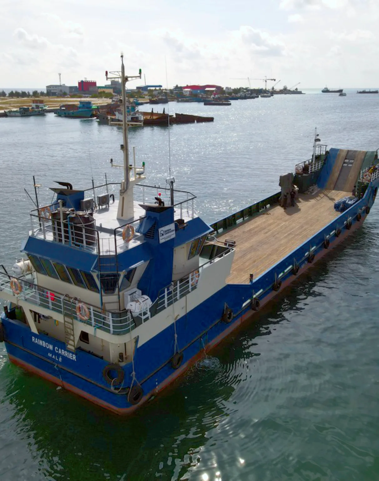 Rainbow's landing craft with its cargo deck, moored in a harbour.