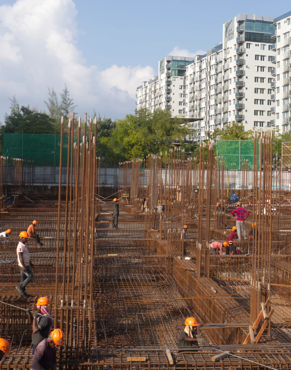 Crew tying reinforcement on a slab under construction, high-rise blocks behind.